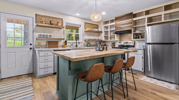 Une cuisine moderne dotée d’un îlot central, de tabourets de bar, d’un réfrigérateur en acier inoxydable et d’étagères en bois.