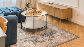 Een moderne woonkamer met een grote bank, een salontafel, een aan de muur bevestigde televisie en een houten kast.