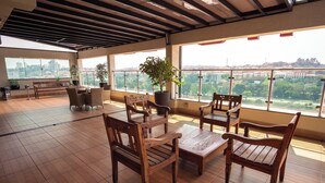 A spacious indoor area with wooden furniture and large windows offering a city view. - Padom Businesse Hotel (Braganca Paulista)