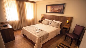 A hotel room with a large bed, two bedside tables, a chair, and a cityscape painting on the wall. - Padom Businesse Hotel (Braganca Paulista)