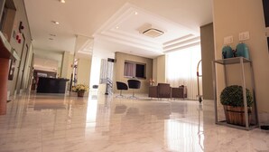 A spacious lobby with a marble floor, a reception desk, seating area, and a potted plant. - Padom Businesse Hotel (Braganca Paulista)