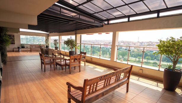 A spacious balcony with wooden flooring, a wooden bench, and potted plants. - Padom Businesse Hotel (Braganca Paulista)