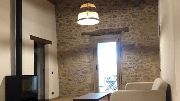 Amplia sala de estar con pared de piedra, techo de madera, mueble de TV negro, sofá blanco y lámpara colgante.
