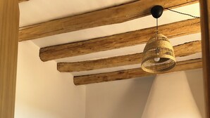 Una habitación acogedora con un sofá blanco, vigas de madera a la vista, una lámpara colgante de fibra y una chimenea de ladrillo con una planta en maceta.