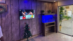 A modern interior with a flat-screen TV mounted on a wooden wall, a small Christmas tree, and a fish tank. - PRESKEN HOTELS FAJODD4 (Lagos)