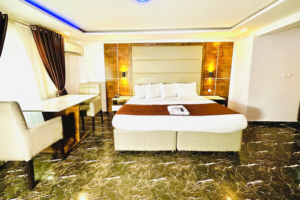 A hotel room with a bed, a desk, a chair, and a marble floor.