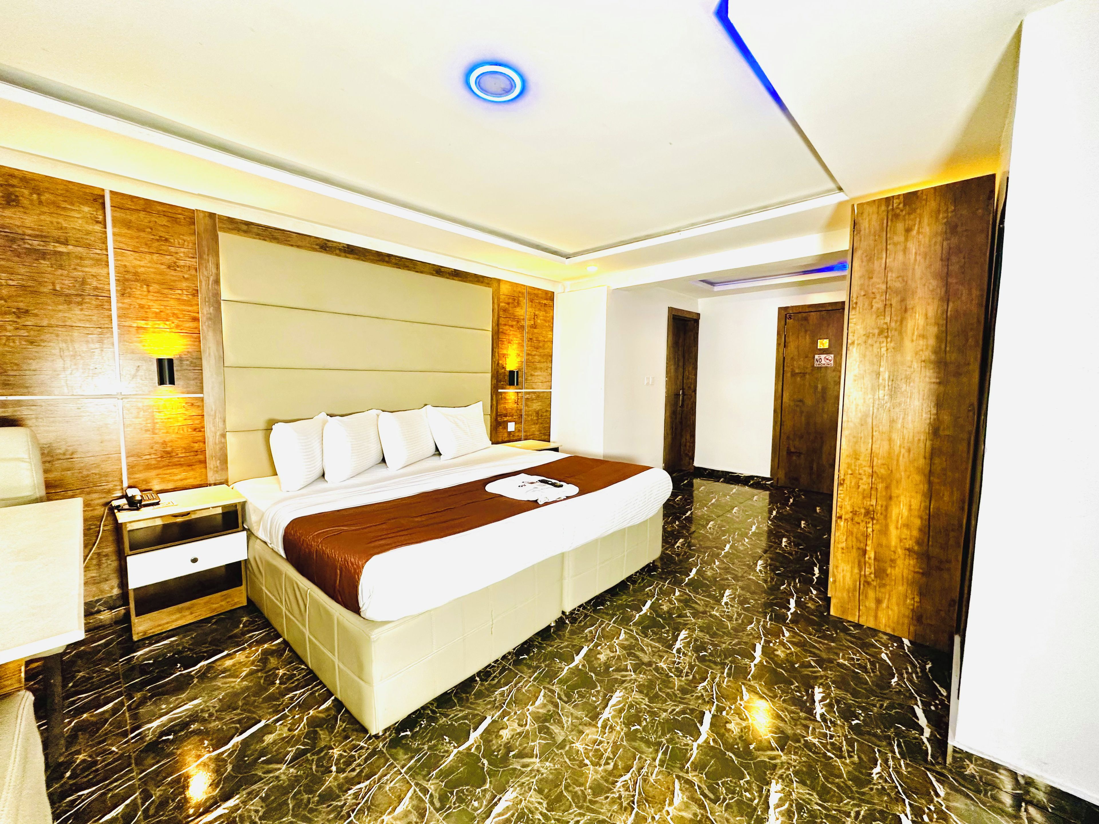 A hotel room with a bed, bedside table, lamp, and a wooden accent wall.