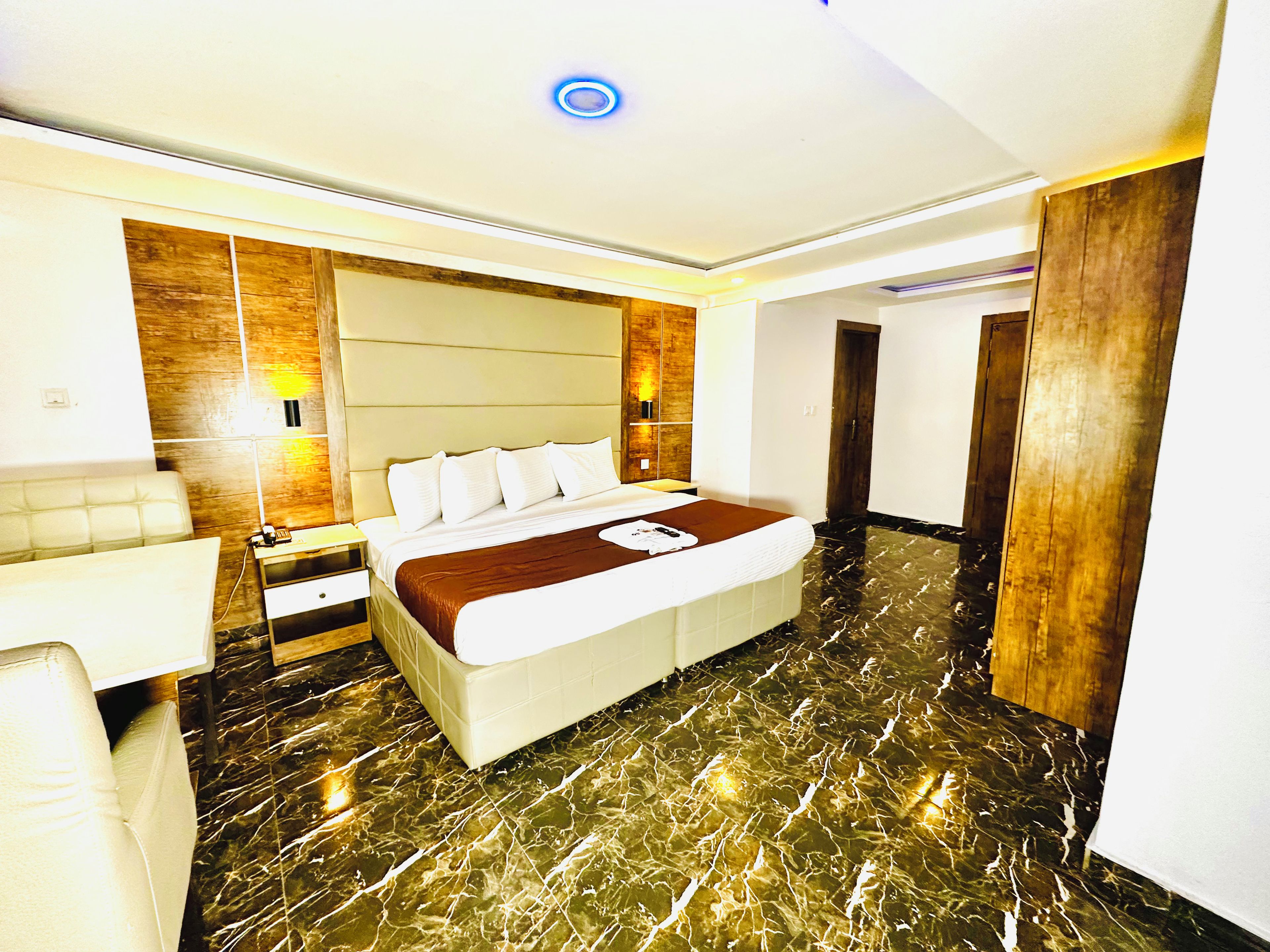 A hotel room with a bed, bedside table, lamp, and a wooden door.
