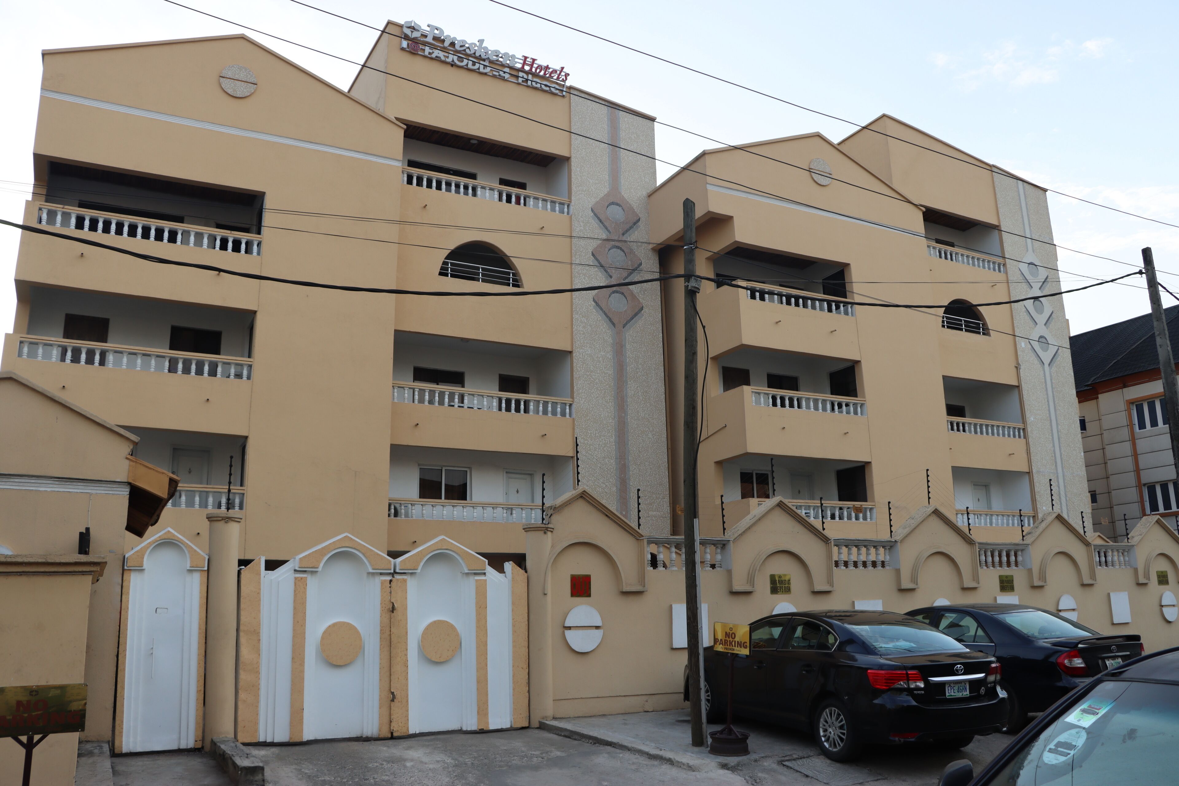 A multi-story hotel with balconies, a gated entrance, and parked cars.
