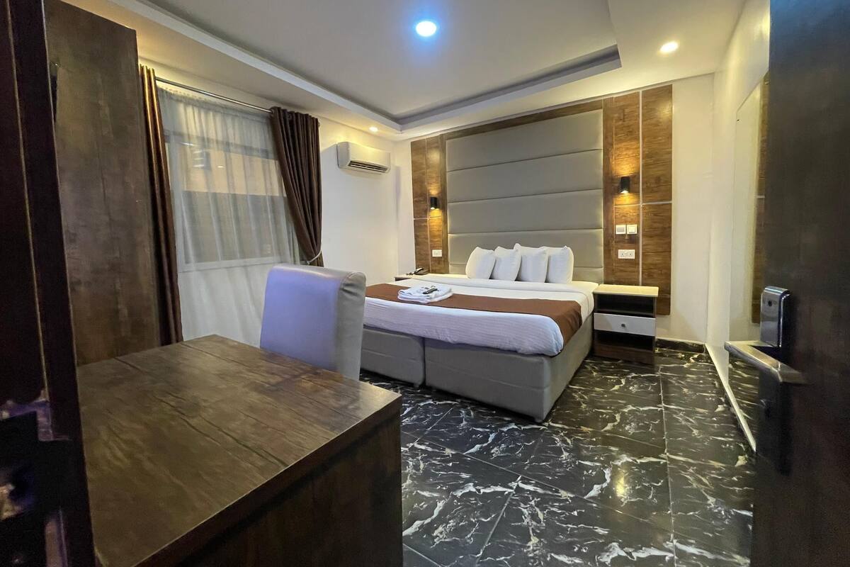 A modern hotel room with a bed, bedside tables, a desk, and a chair.