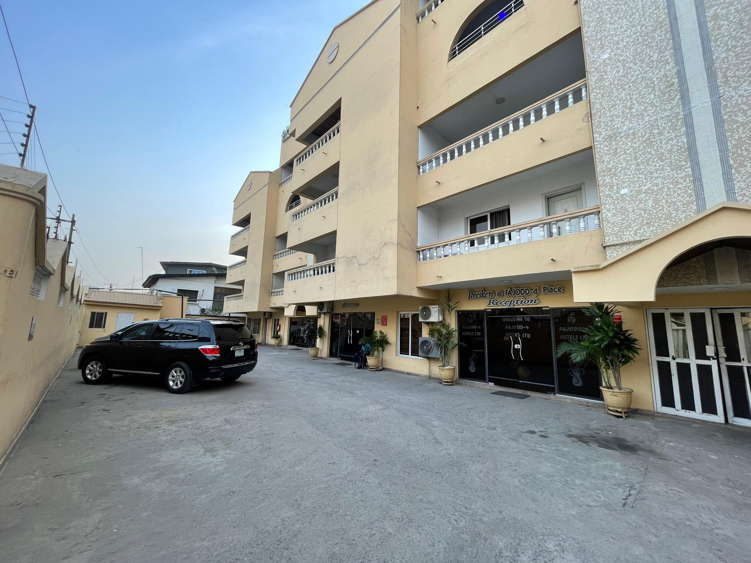 A hotel with a reception area, multiple balconies, and a parking lot with a black car.