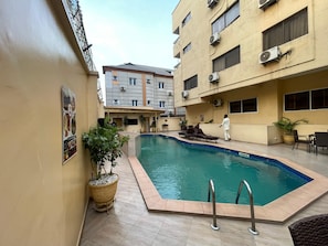 A swimming pool area with a tiled deck, lounge chairs, and a potted plant. - PRESKEN HOTELS FAJODD4 (Lagos)