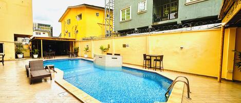 A swimming pool with a tiled deck, surrounded by a building with multiple windows and balconies.