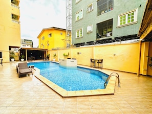 A swimming pool with a tiled deck, surrounded by a building with multiple windows and balconies. - PRESKEN HOTELS FAJODD4 (Lagos)