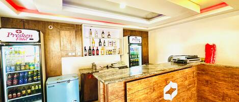 Een hotel receptie met een houten balie, twee drankdispensers en een wandplank voor sterke drank.