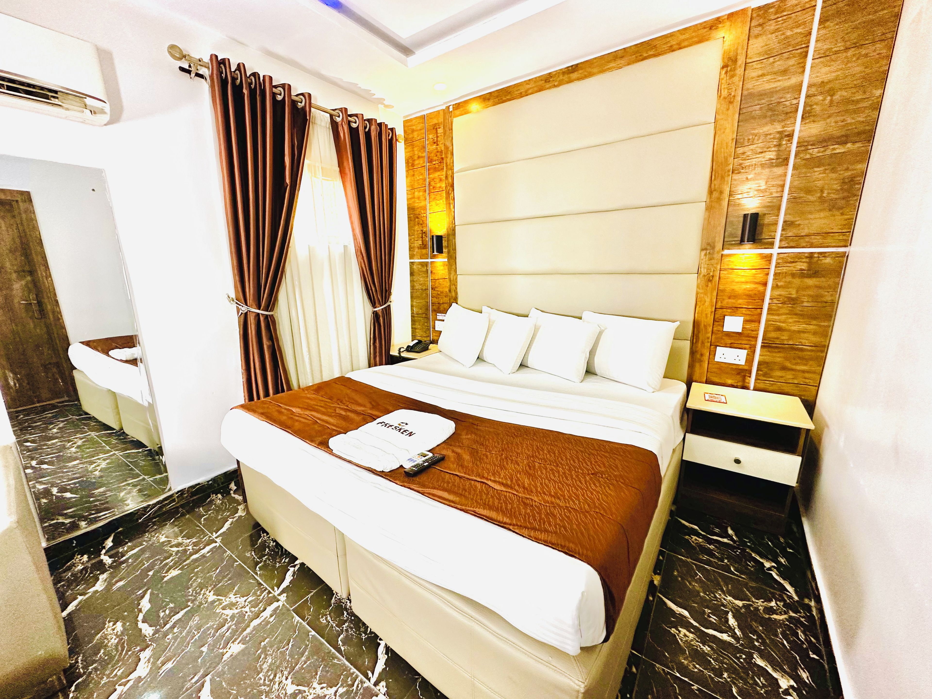 Une chambre d’hôtel comprenant un lit, une table de chevet, une commode, un miroir et une salle de bain avec des toilettes et un lavabo.