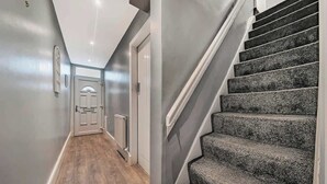 Un pasillo con suelo de madera, pared gris y una escalera con peldaños alfombrados en color gris.