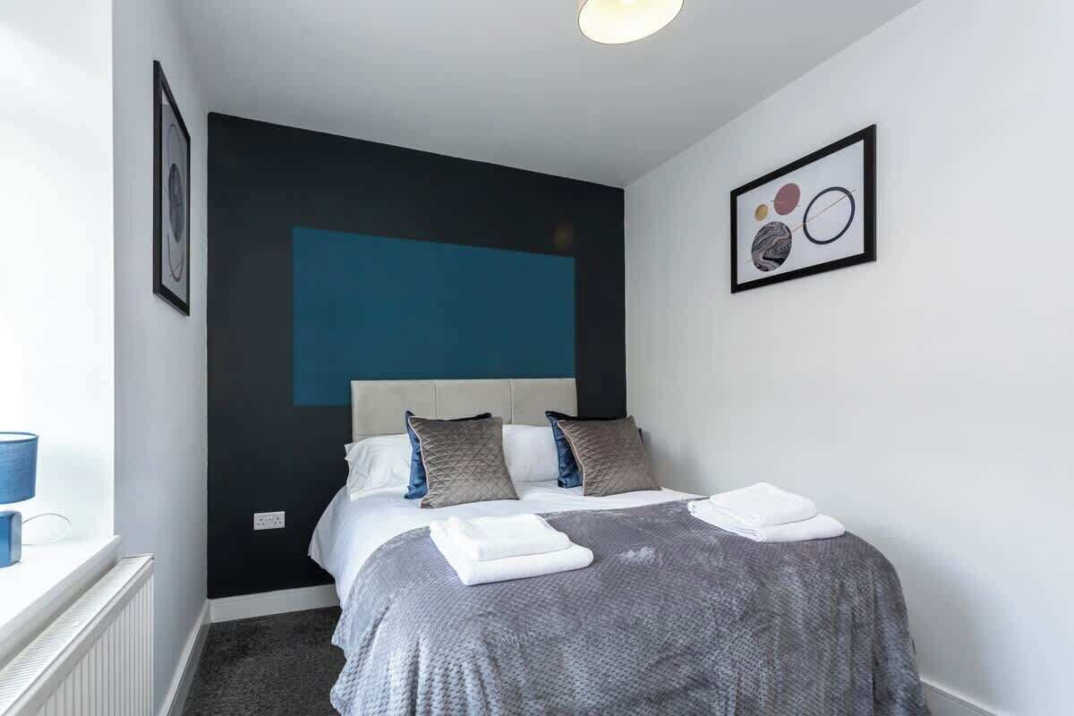 A modern bedroom with a large bed, a blue accent wall, and a framed abstract art piece.