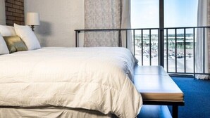 A hotel room with a large bed, a bench, a lamp, and a view of the city through large windows. - The Landmark Hotel (Laredo)