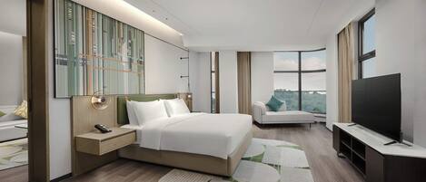 A modern hotel room with a large bed, a TV, a seating area, and a city view.