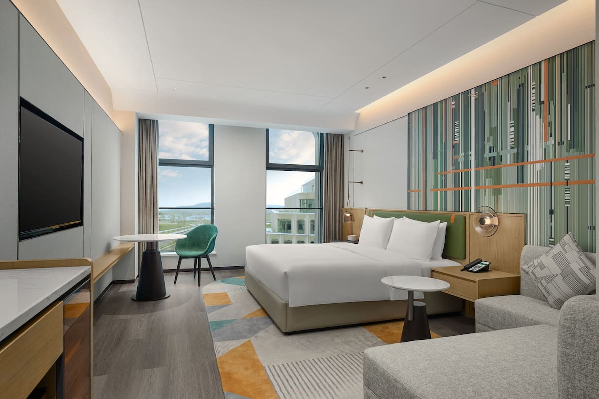 Una camera d'hotel moderna con un letto grande, una scrivania, una sedia, un tavolino e vista sulla città.