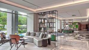 Een moderne hotellobby met een zithoek, een glazen scheidingswand met planken en uitzicht op het omliggende landschap.