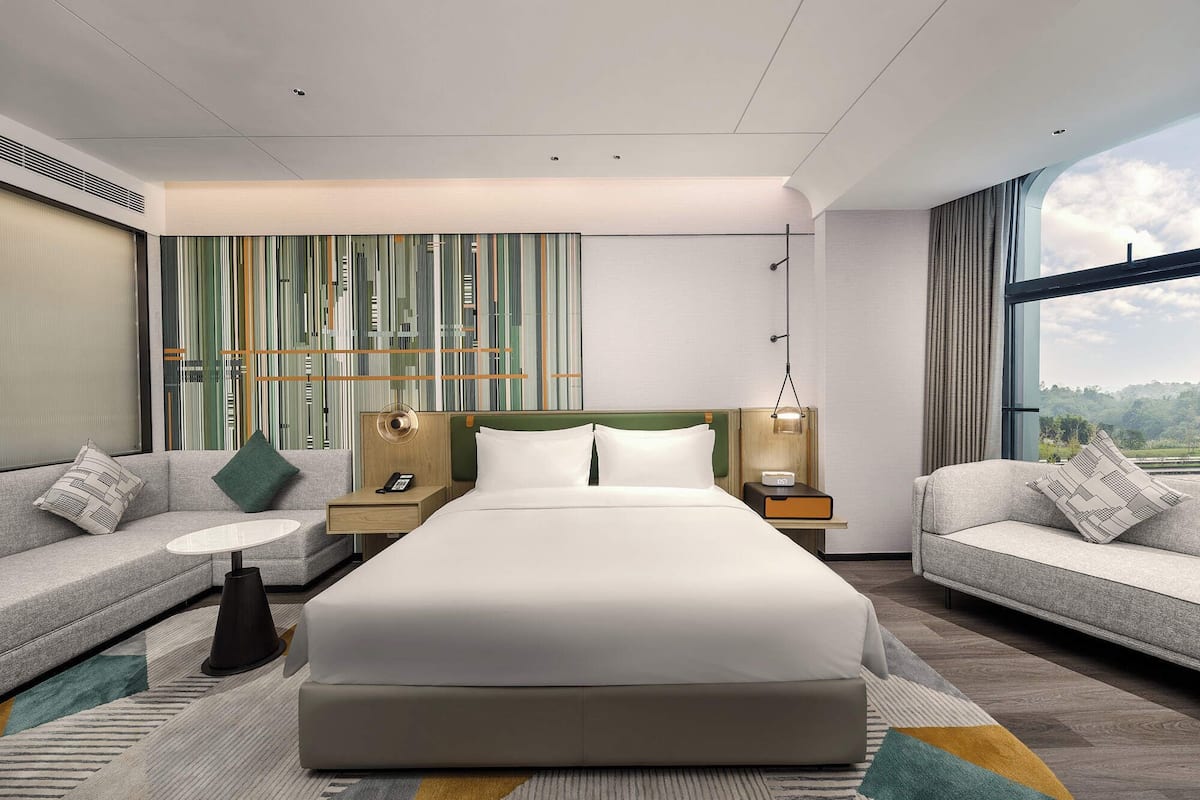 Una camera d'albergo moderna con un letto grande, due divani, un tavolino e vista sull'esterno.