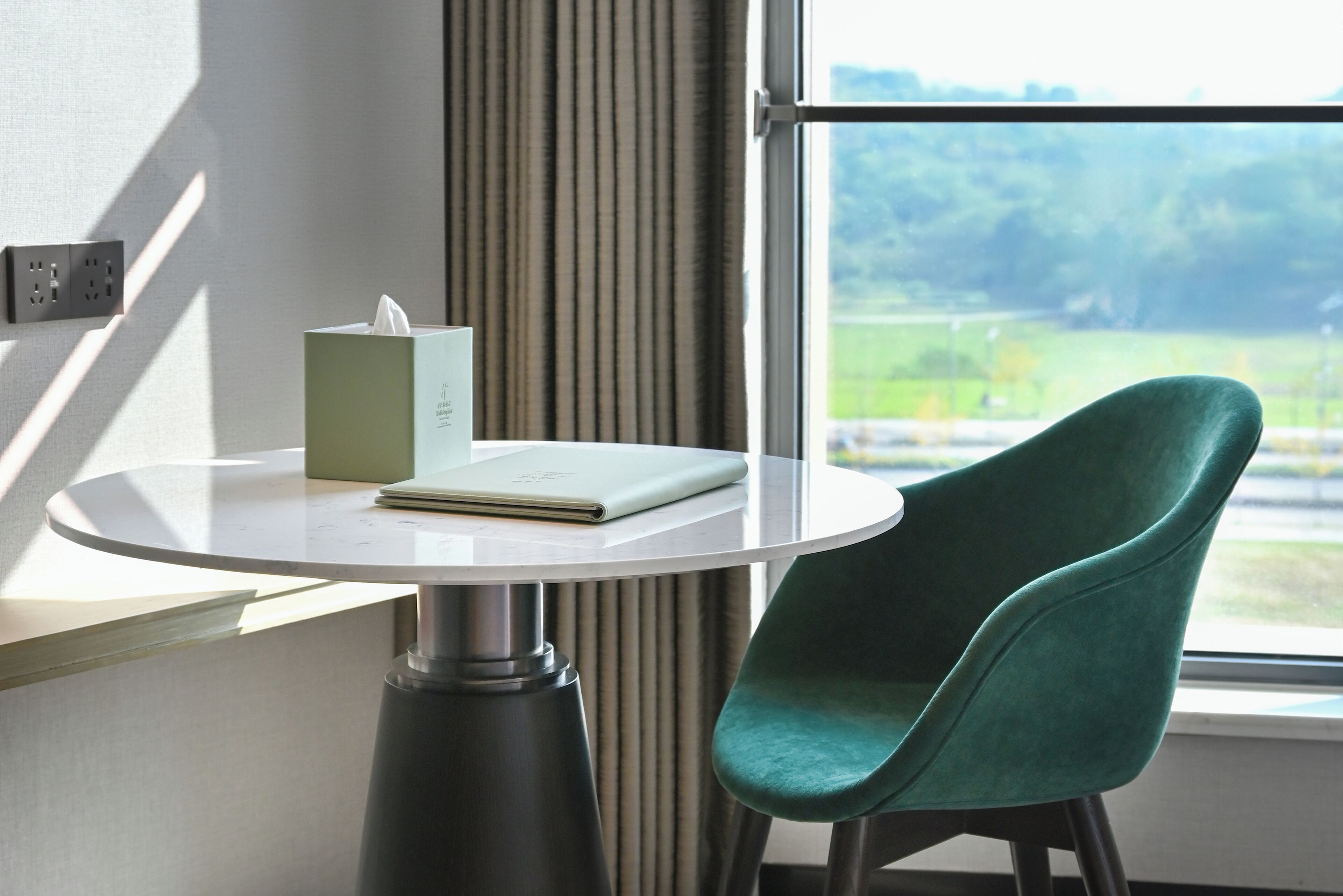 A room with a round table, a green chair, a tissue box, and a notebook.
