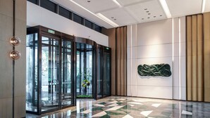Een moderne lobby met een glazen ingang, een vloer met een geometrisch patroon en een abstract kunstwerk aan de muur.