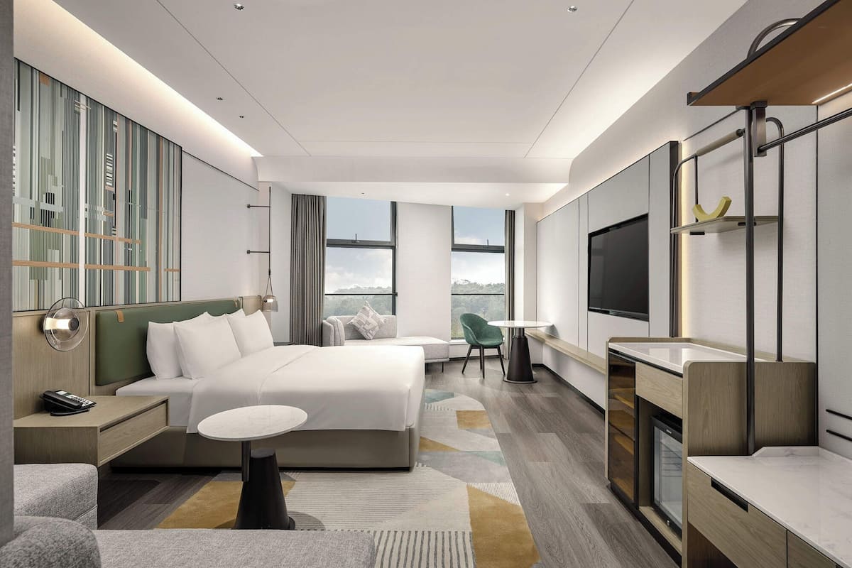 Camera d'hotel moderna con un letto grande, una scrivania, una sedia, una TV e vista all'esterno.
