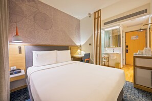 Hotellihuone, jossa on sänky, yöpöytä, lamppu sekä kylpyhuone, jossa on pesuallas ja peili.