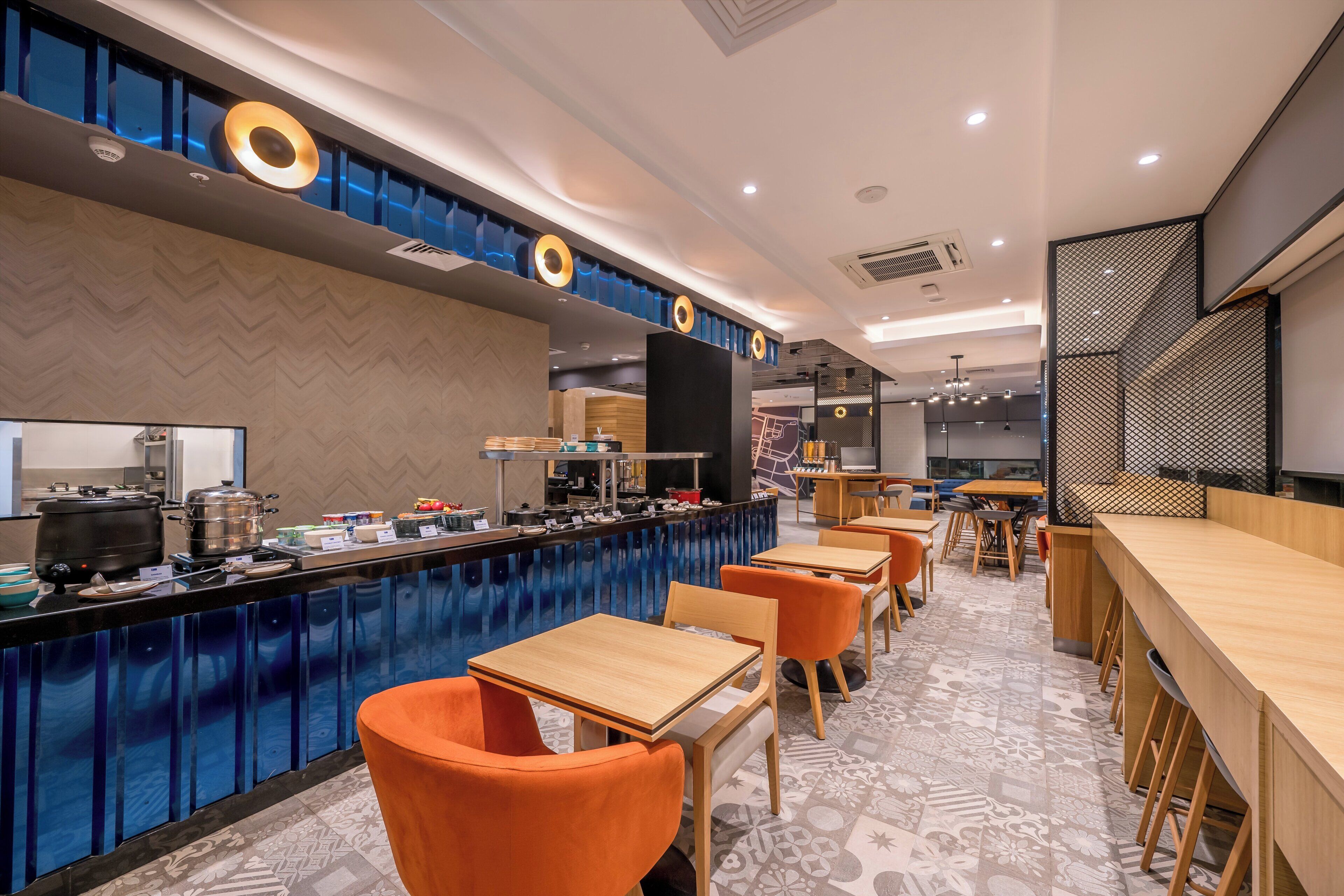 A modern restaurant with a bar area, wooden tables, and orange chairs.