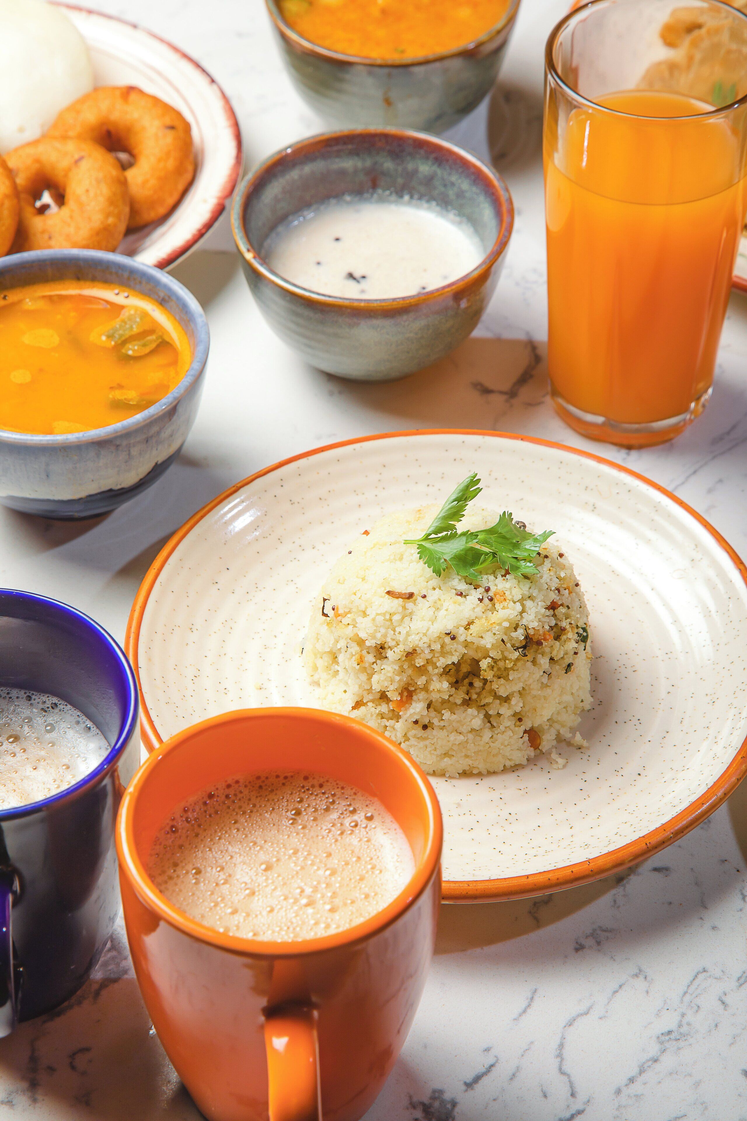 Una mesa con un plato de arroz, tazones de sopa, un vaso de jugo de naranja y dos tazas.