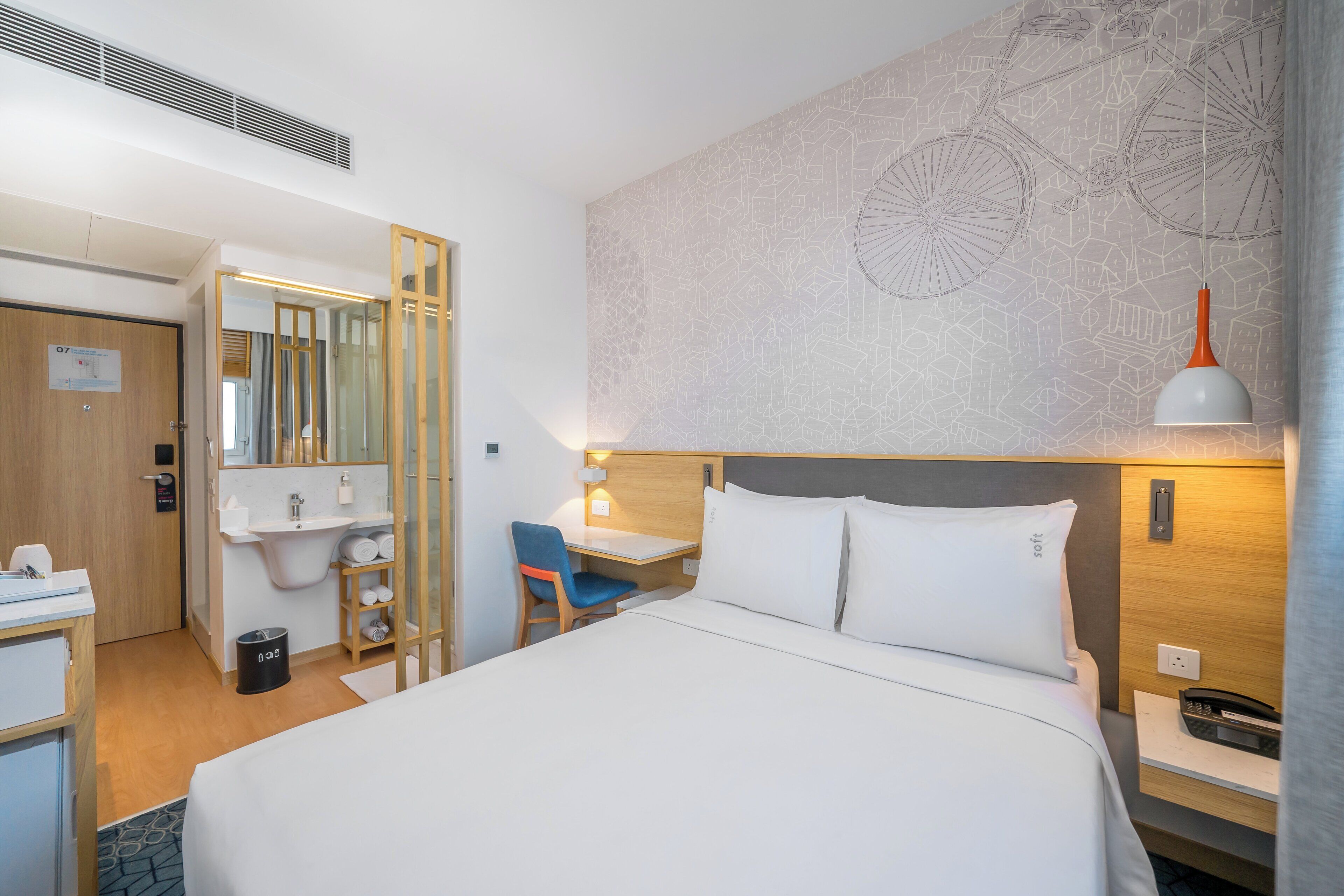 A hotel room with a bed, a desk, a chair, a sink, and a mirror.