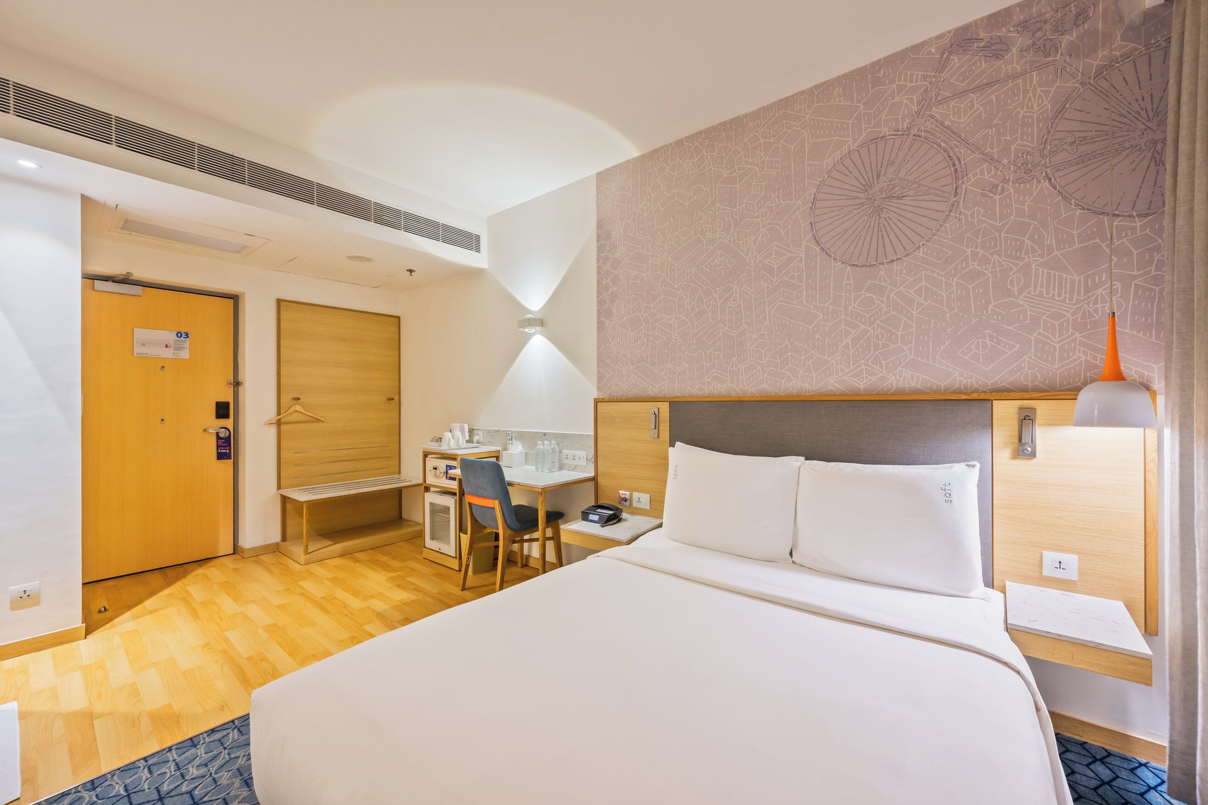 A hotel room with a large bed, a desk with a chair, a small kitchenette, and a bathroom door.