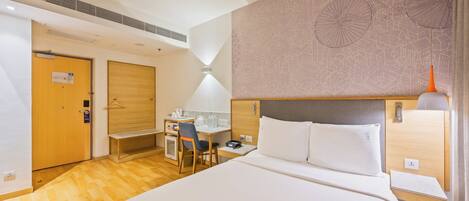 A hotel room with a large bed, a desk with a chair, a small kitchenette, and a bathroom door.