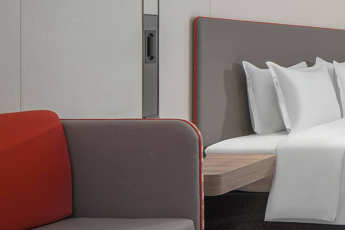 A modern hotel room with a grey sofa, a wooden nightstand, and a bed with white linens.