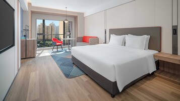 Un hotel moderno con una cama grande, un balcón con una silla roja y vistas a edificios altos.
