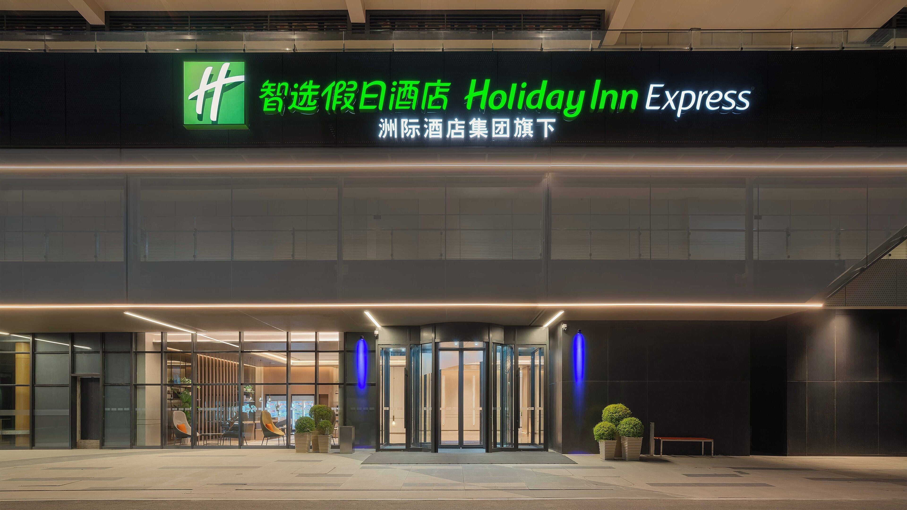 A Holiday Inn Express hotel entrance with a modern design, glass doors, and a visible outdoor seating area.