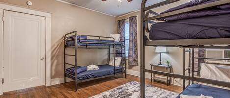 A dormitory room with bunk beds, a ceiling fan, a door, and a window with curtains.