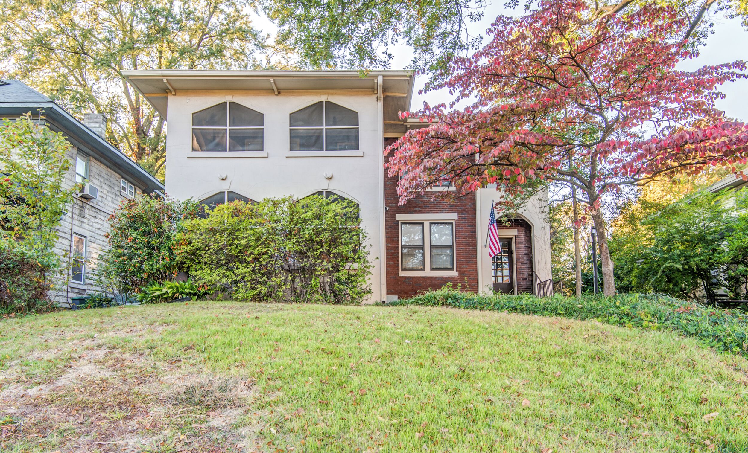 A two-story house with a front yard, a brick entrance, and a large tree with pink leaves.