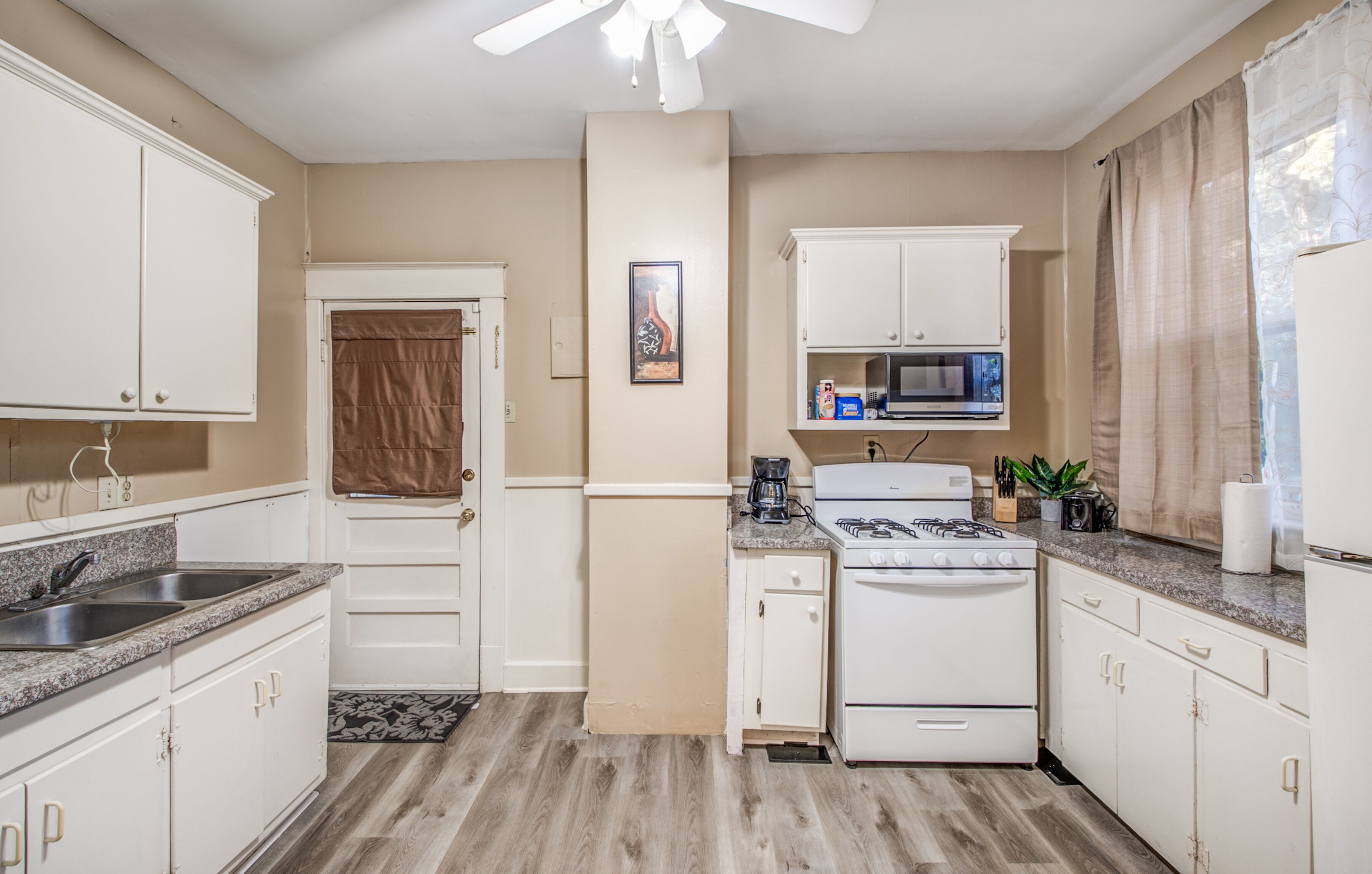 A compact kitchen with white cabinets, a gas stove, a microwave, and a sink.