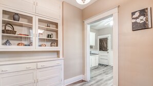A hallway with a white cabinet displaying various items, a wooden floor, and a door leading to another room. - Bluemoon Bungalow 2 Units (Memphis)