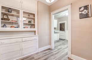 A hallway with a white cabinet displaying various items, a wooden floor, and a door leading to another room.