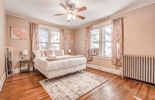 A bedroom with a large bed, a ceiling fan, and a radiator.