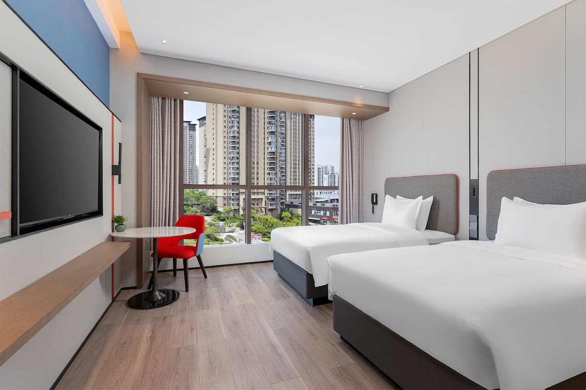 A hotel room with two beds, a TV, a small table, and a red chair.