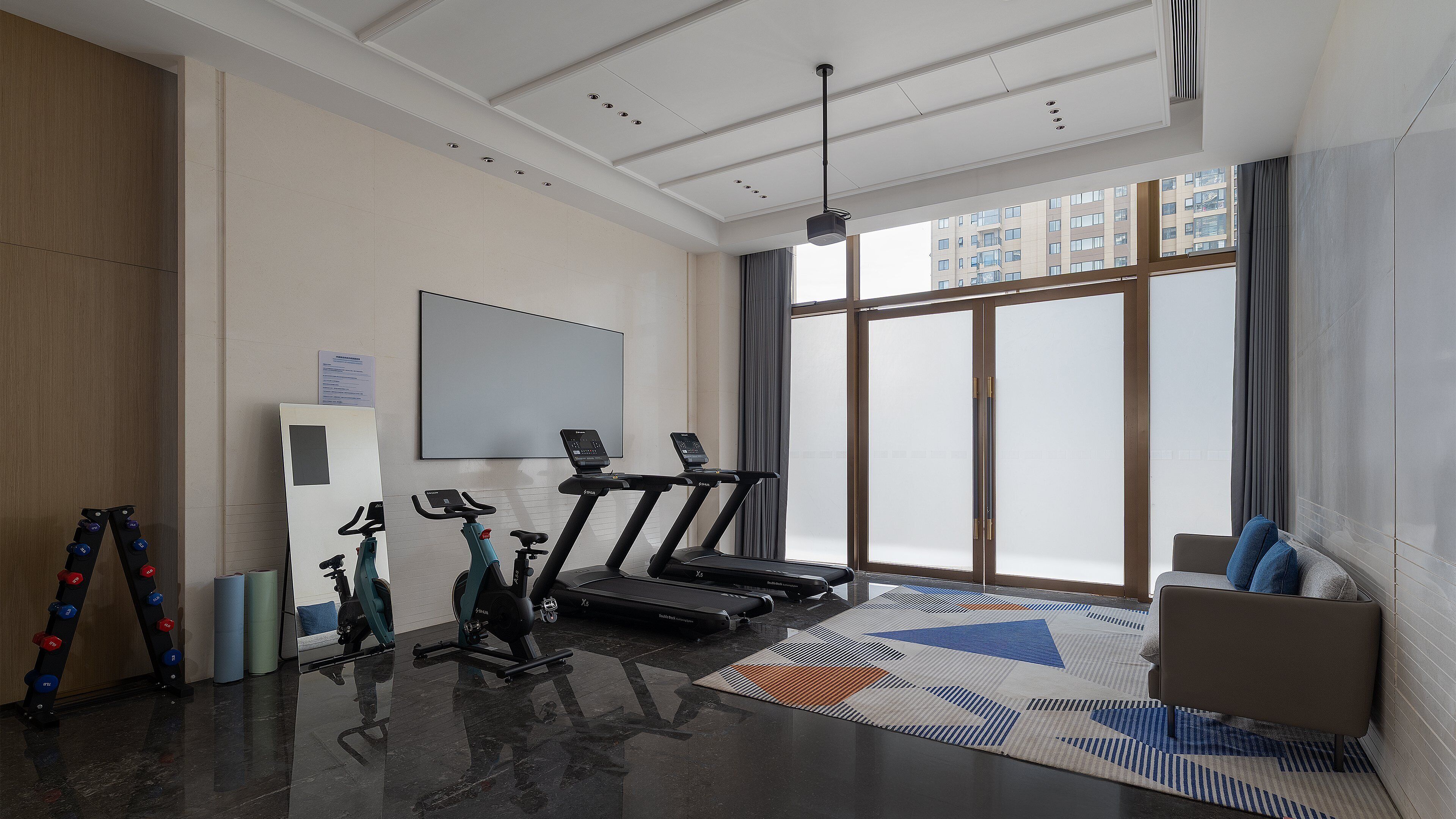 Un gimnasio moderno con equipo de ejercicio, un ventanal grande y vistas a un edificio.