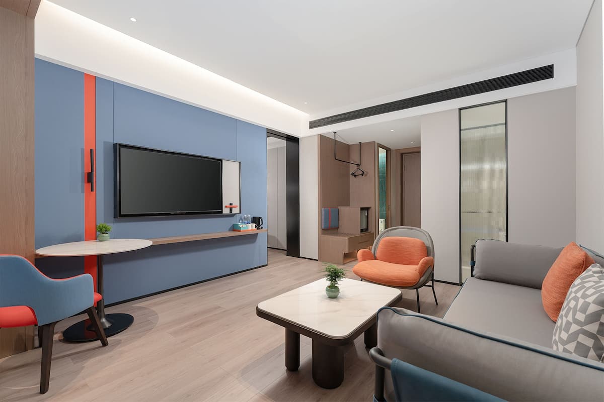 A modern living room with a flat-screen TV, a round coffee table, and a sofa with orange cushions.