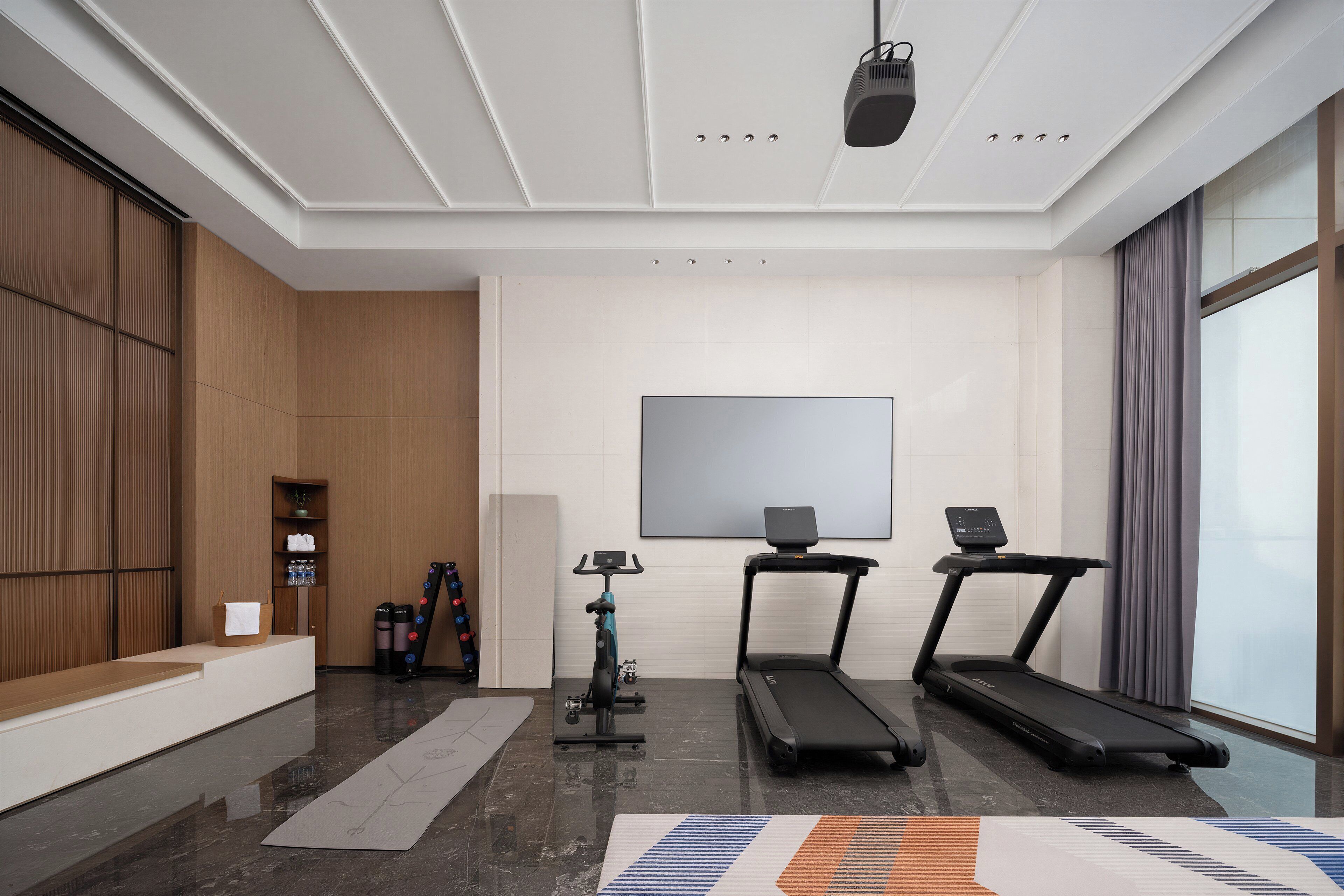 A modern gym with a treadmill, stationary bike, and a large screen.