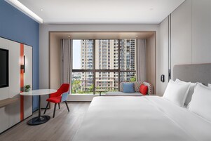 Una habitación de hotel moderna con una cama grande, una silla roja, una mesita pequeña y un televisor.
